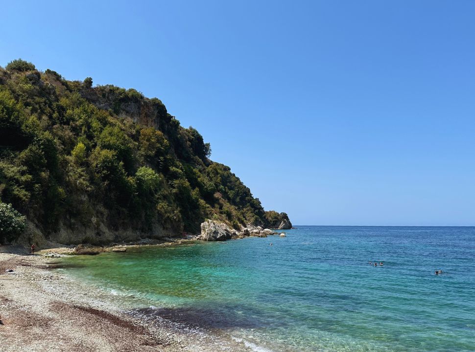 turquoise blue water at the end of a beach with a cliff covered with vegetation in Himare Albania