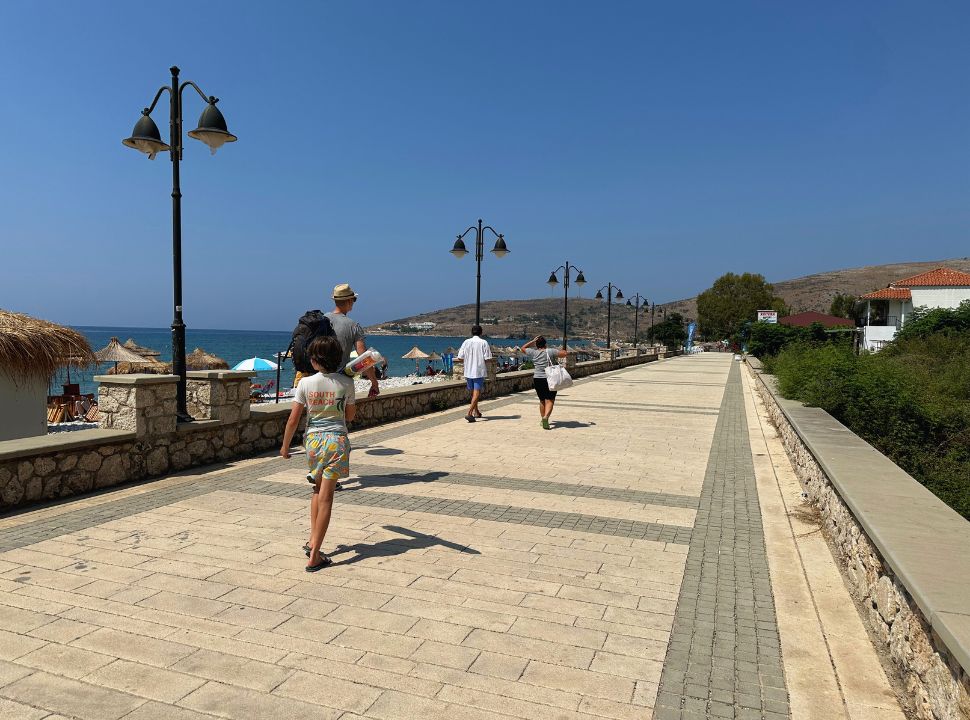 father and son walking along the boulevard with the beach on the left side, and a small accommodation on the other at Qeparo Beach Albania