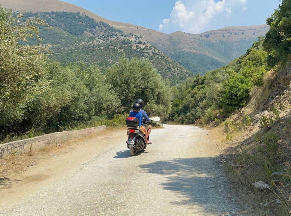 father and son driving a motorscooter from the beach back to the main road, towards the mountains at Buneci Beach Albania