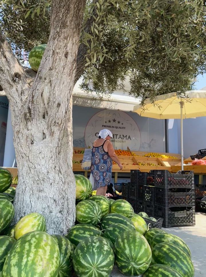 woman with small towel on her head to cool her off while shopping at a food stall in Albania