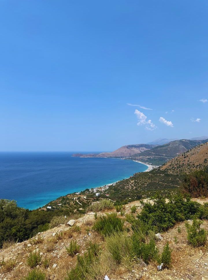 view of the bay with a long stretched beach with stunning blue water surrounded by mountain landscape 