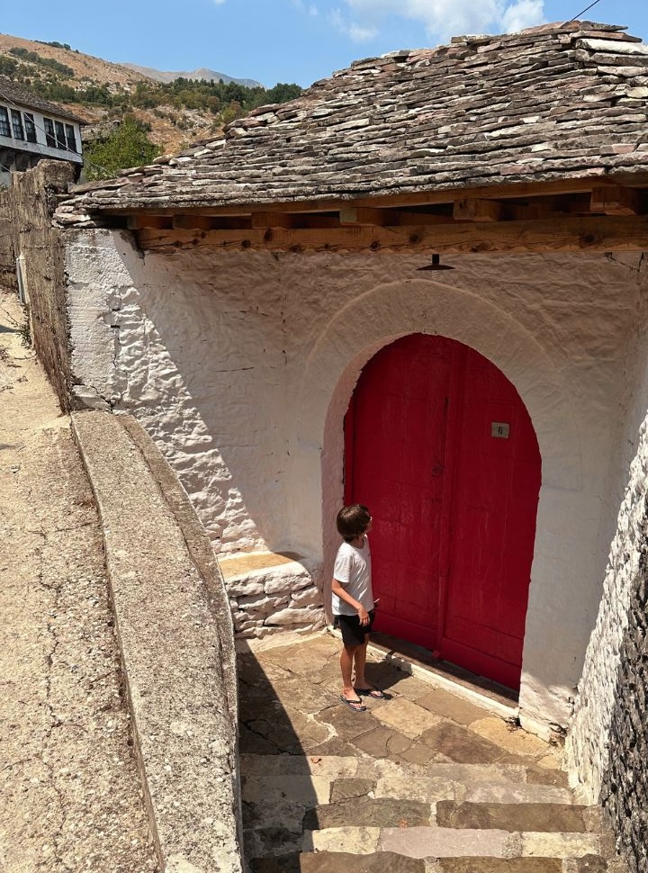 boy standing at a red old door at a typical stone entrance at Gjirokaster Albania