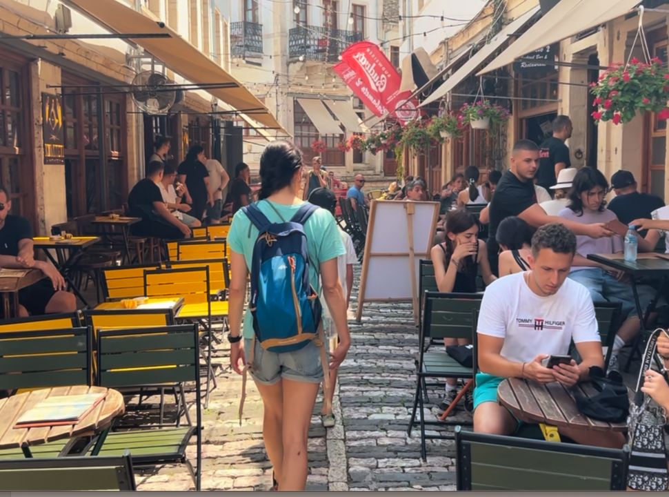 woman walking through a street full with restaurants and people sitting outside in Gjirokaster Albania