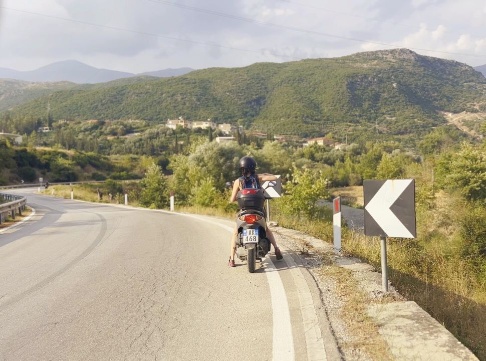 woman on motor scooter stopping at the side of the road to take a picture of the mountain landscape near blue eye Albania