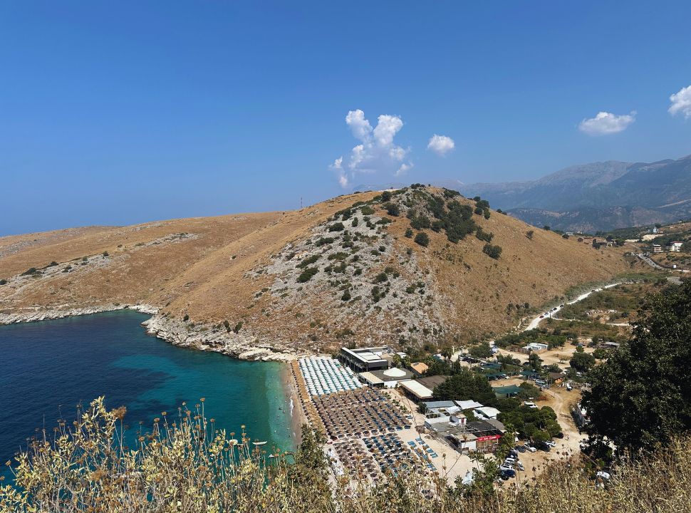 small bay with little beach set along stunning water, mountain back drop in Albania