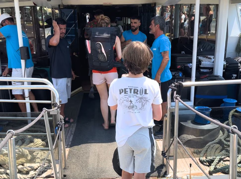 boy boarding the Corfu Albania ferry where a couple of crew are ready to help him with his luggage 