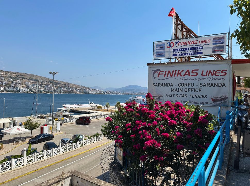 sign of a ferry company with in the back the ocean and the town Sarandë Albania