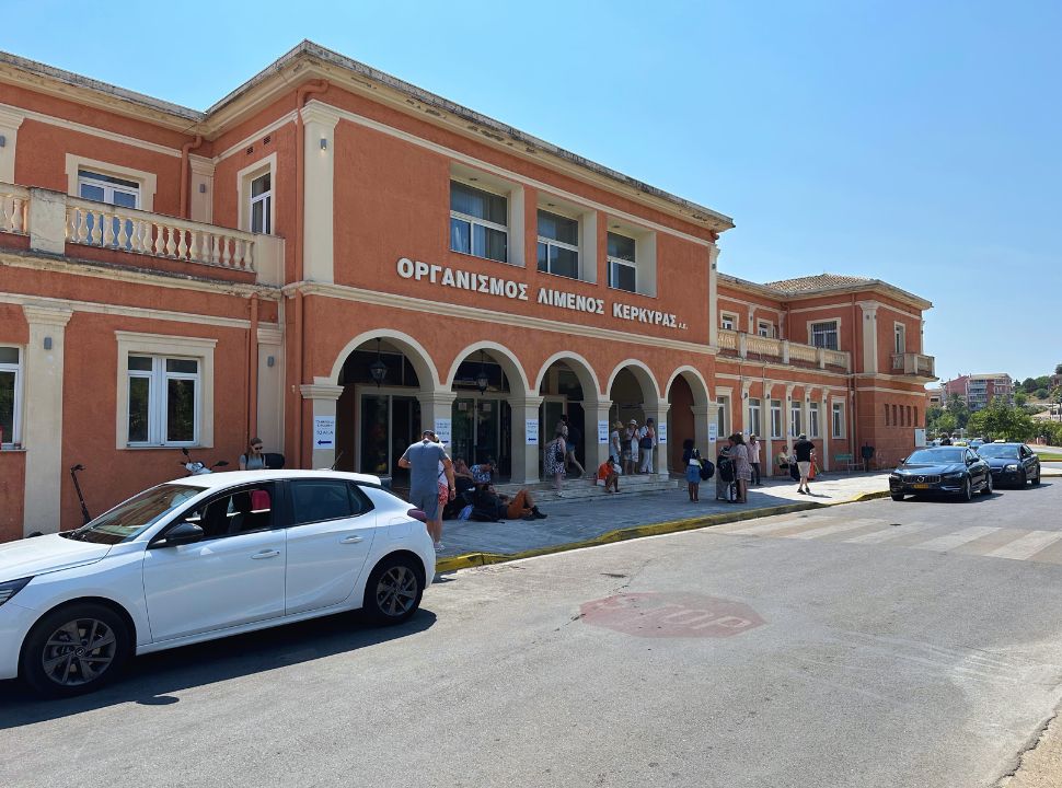 red stone coloured building of the Corfu Port where people are standing outside, waiting to depart