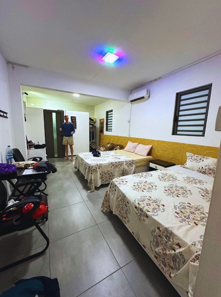 man standing in a room with double beds, tiled floors, and colorful lighting. Not a very charming room in Mauritius.
