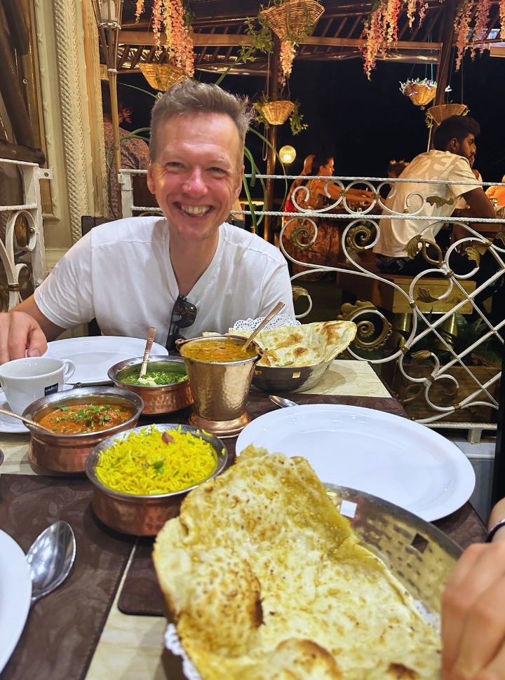 man having dinner at an indian restaurant, table is filled with naan bread, yellow rice, curries and dahl in Mauritius