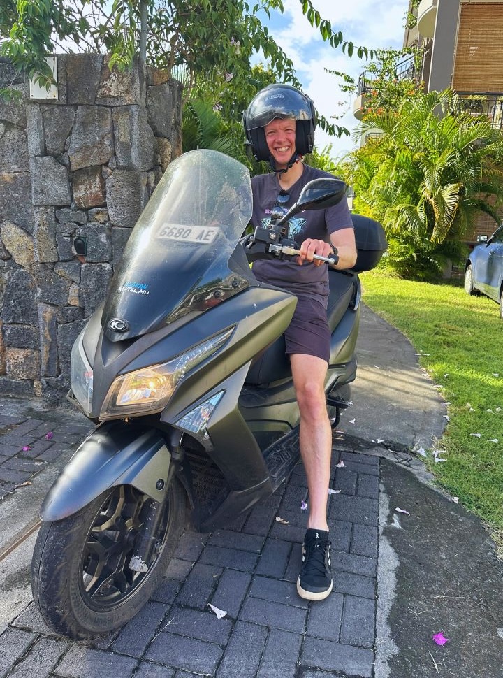 man standing with a kymco motorscooter in a tropical garden at a hotel in Mauritius