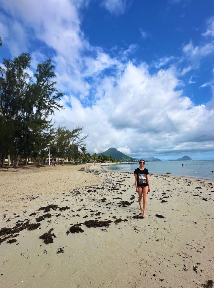 woman walking along a deserted tropical beach in Mauritius that has trees and a calm blue ocean, mountains are visible in the back