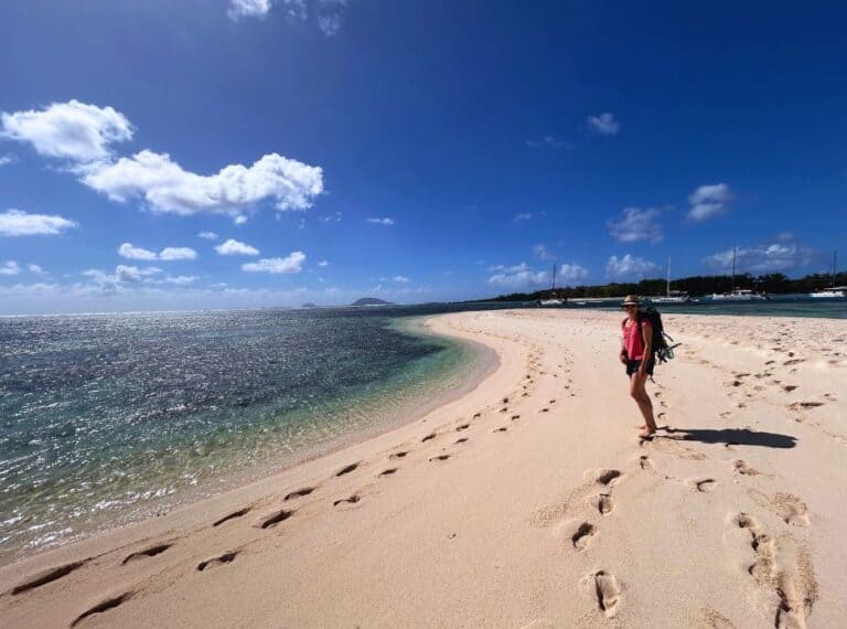 woman standing on a tropical white sanded beach with clear turqoise water