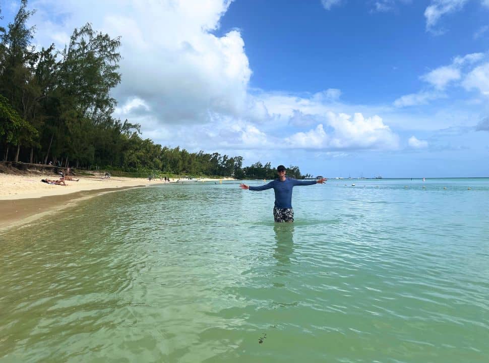 man posing happily in the water at a long stretched beach with lush vegetation in Mauritius