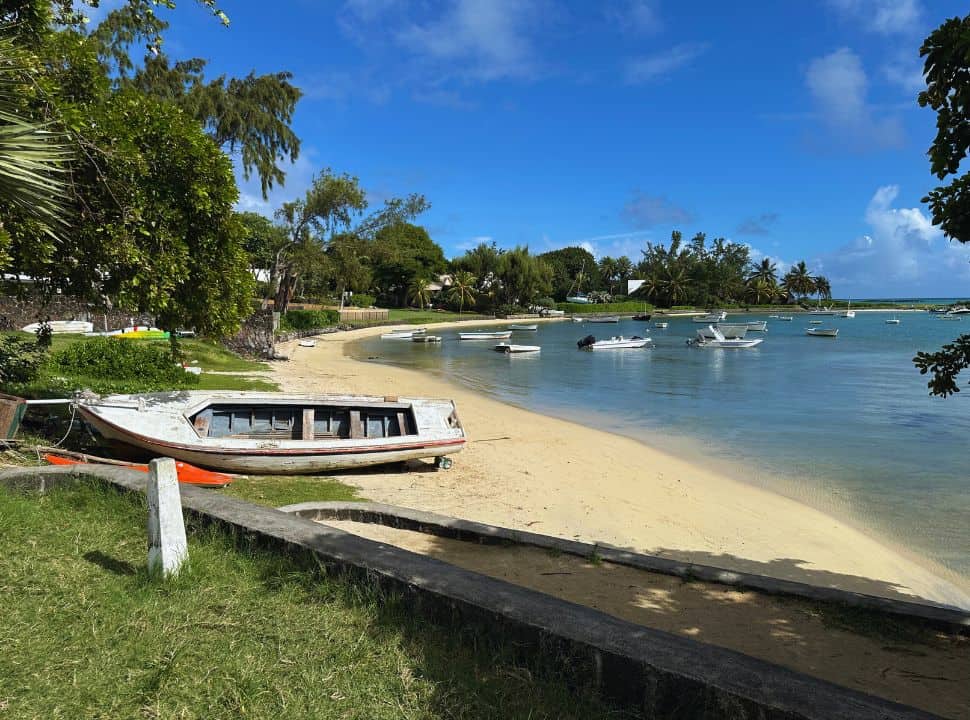small beach with boats at the water front and one lying on its side on the beach, trees are set in the grass right at the beach in north Mauritius