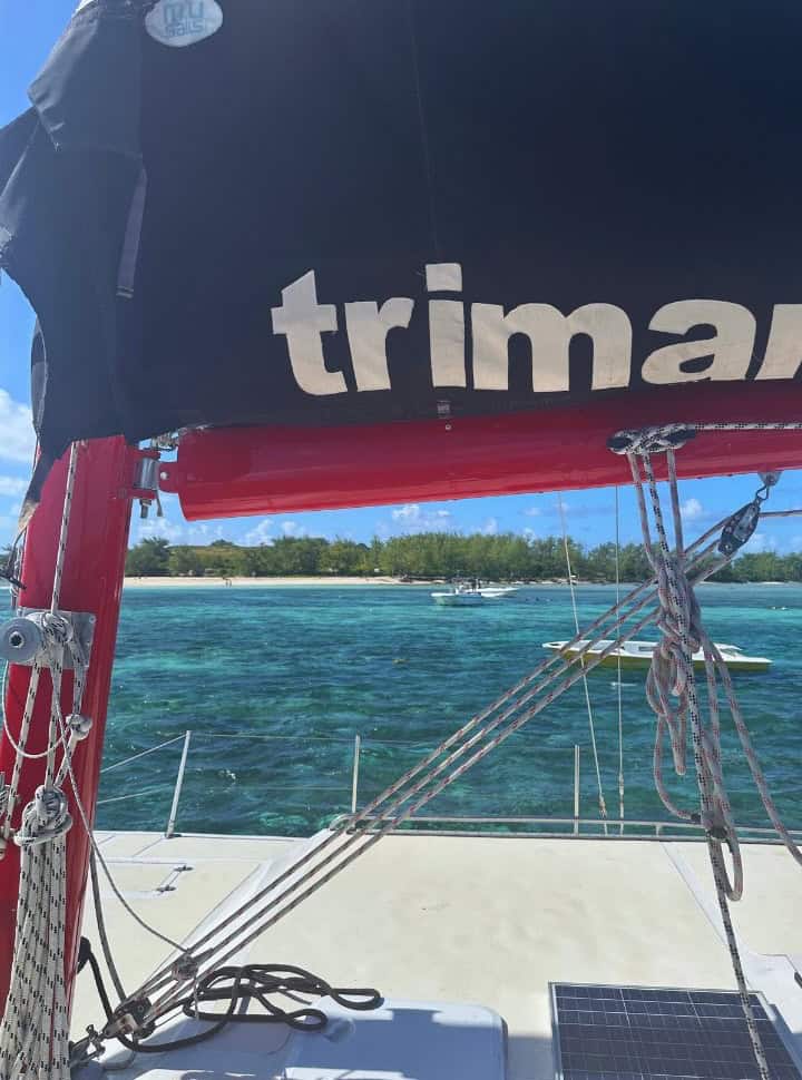 picture taken from a catamaran, the sail is partly visible in the back you have an island with a white beach and green vegetation located just north of Mauritius