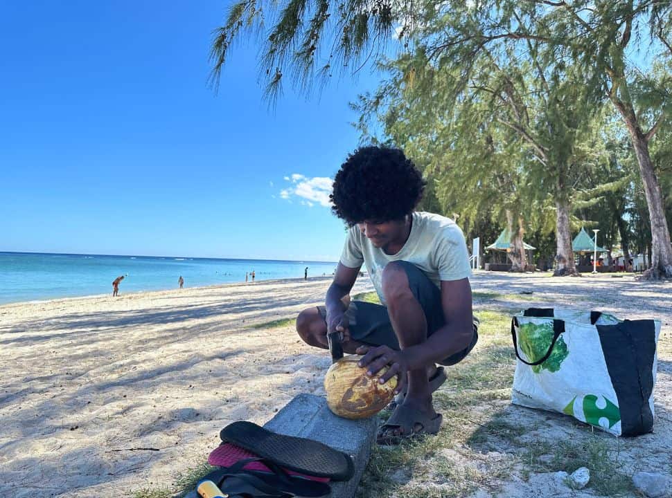 man cutting a coconut open at the edge of the beach at Flic en Flac Mauritius