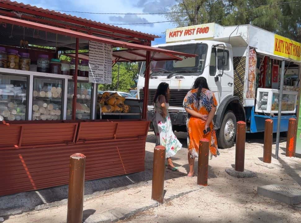 two woman standing in the shade of the food trucks at Flic en Flac waiting for their order