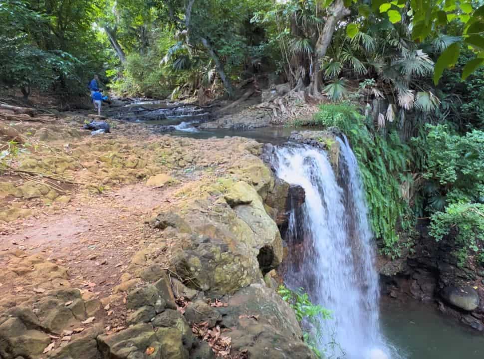 father and son walking along the river that flows straight into a waterfall, surrounded by lush vegetation in Mauritius