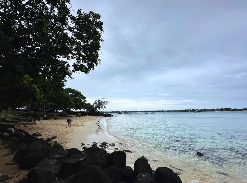 a cloudy sky above a deserted little beach where a father and boy are playing along the water edge in Mauritius