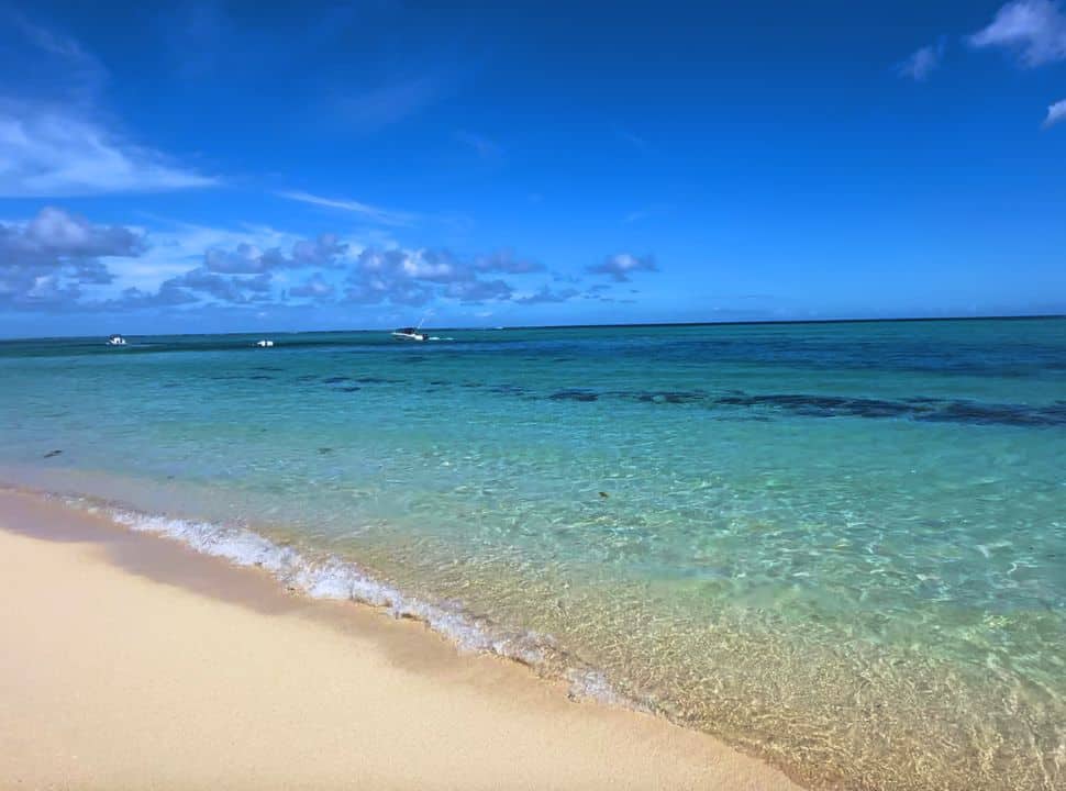 clear ocean water in the colours blue, turquoise, blue and emerald. This Mauritius beach has soft sand, boats cruising in the distance