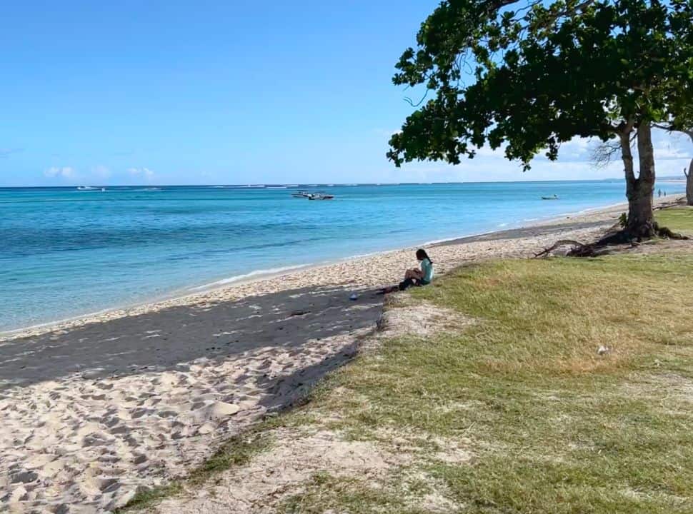 woman sitting in the shade of a tree at a white sanded beach in Mauritius with bright blue ocean