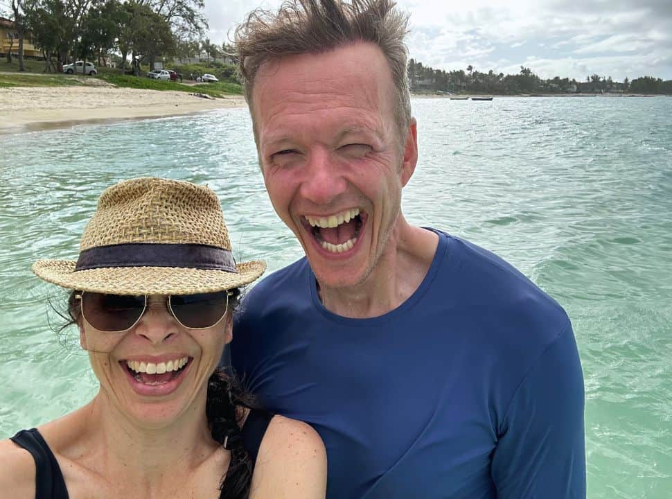 a man and a woman taking a selfie while laughing out loud at a overcast beach