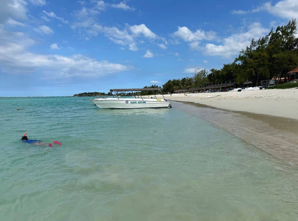boy snorkeling in the water, a boat is anchored at the beach front where rows of sun umbrellas are found owned by a Palmar beach resort