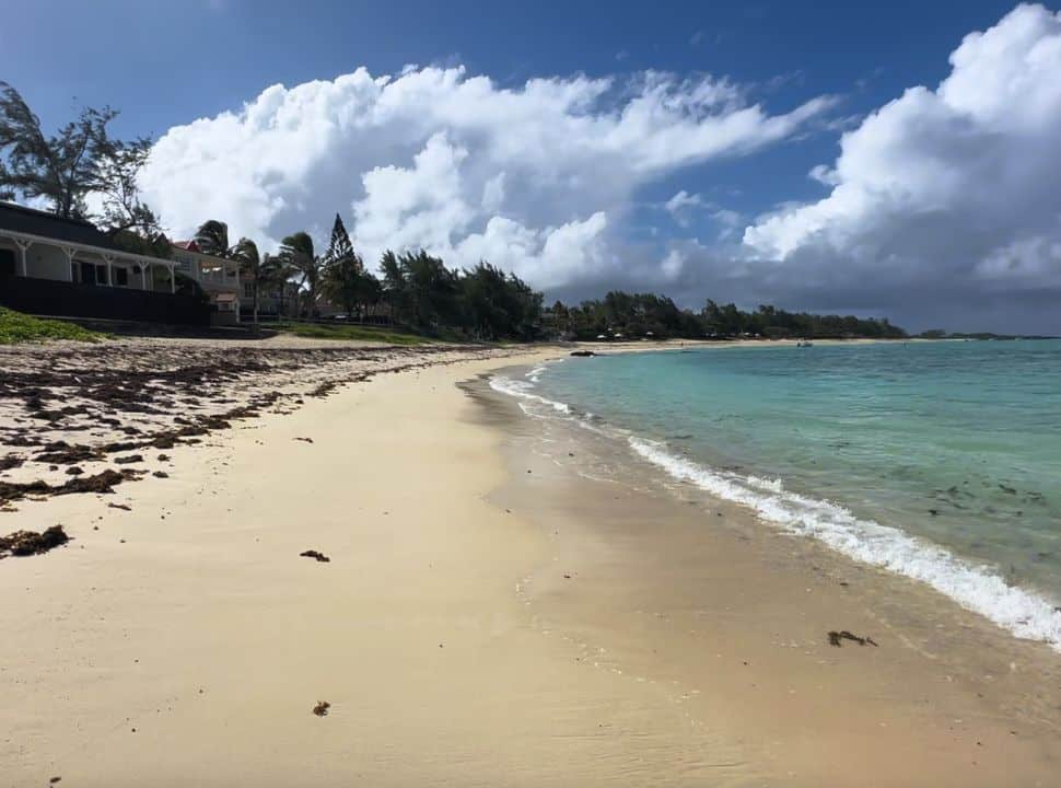 long stretched beach with soft sand, some seaweed along the beach and houses at the beach front along the east coast of Mauritius