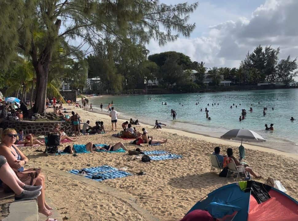 very busy beach, people are lying on the beach, others a swimming in the water, it is cloudy at Pereybere beach Mauritius