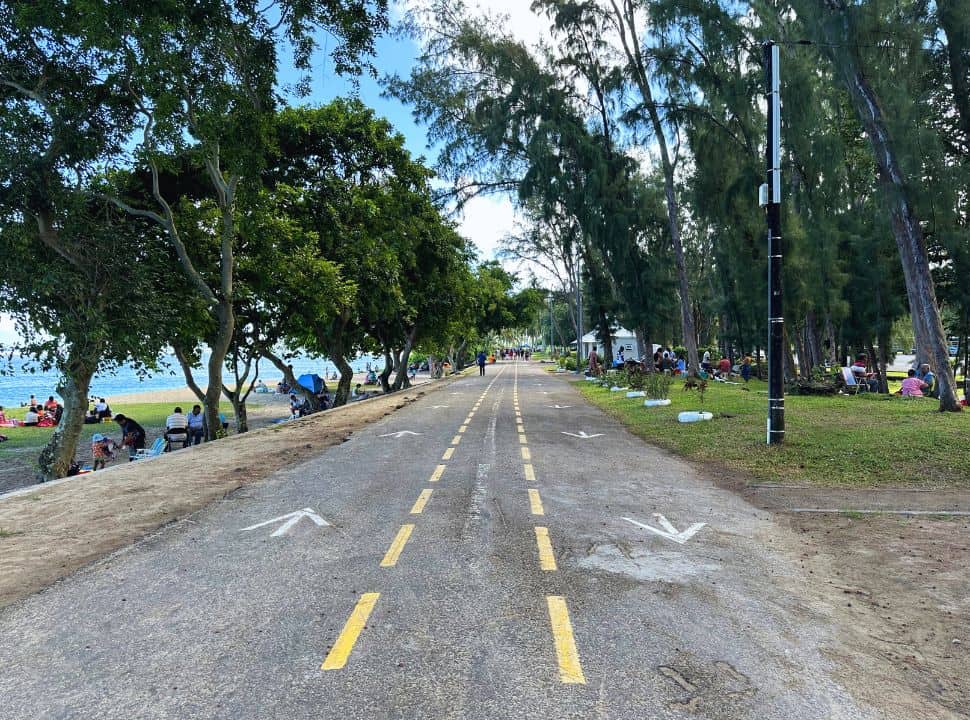 small walk way crossing the park with one side the park itself and the other the beach. People are gathered and enjoying the setting in Mauritius