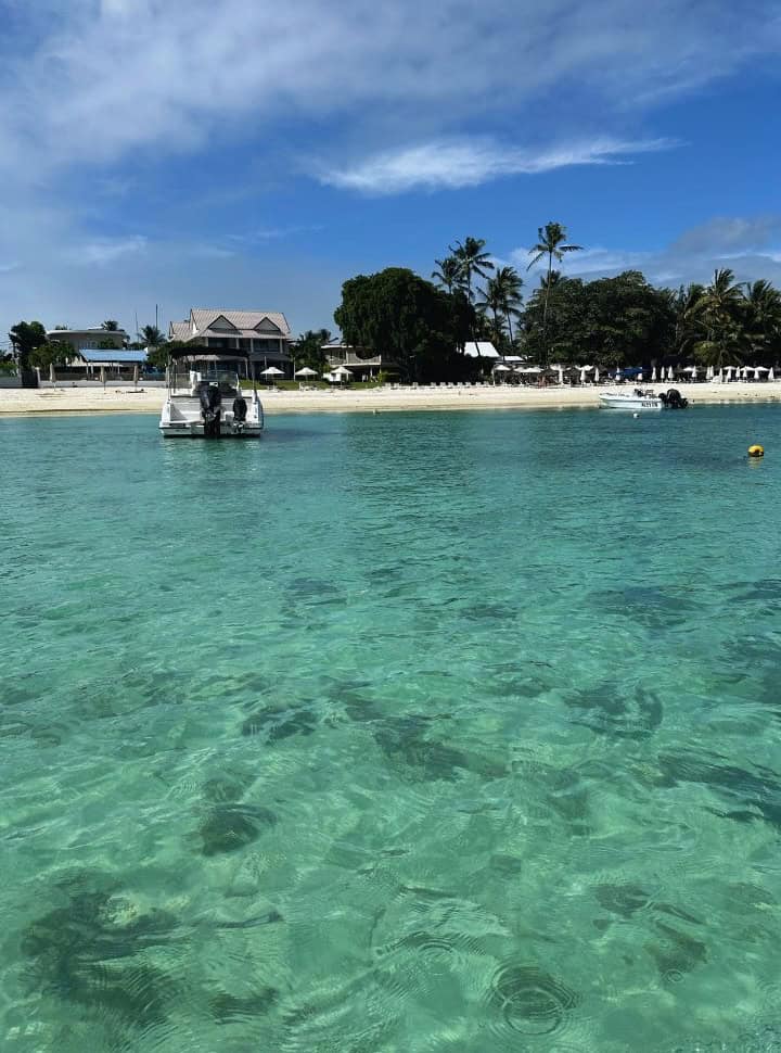 clear turquoise water at a white sanded beach with a hotel and row of sun beds, a boat is anchored just off shore at on of the best beaches in Mauritius