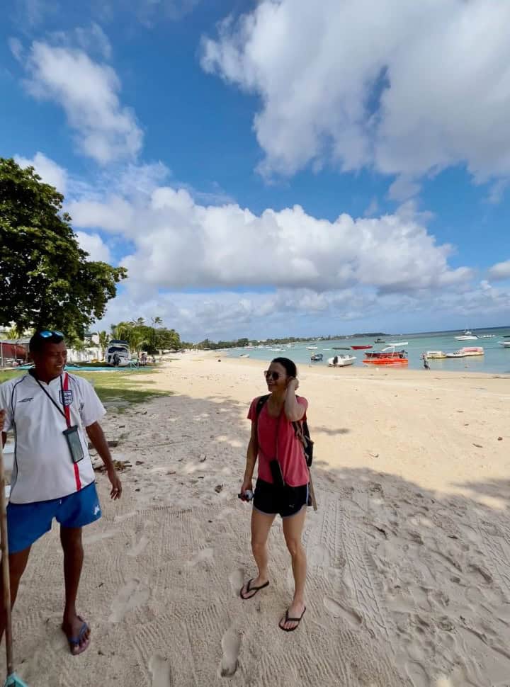 woman talking to a man who is selling tours at the beach, in the back small boats are anchored right at the beach shore at trou aux biches Mauritius