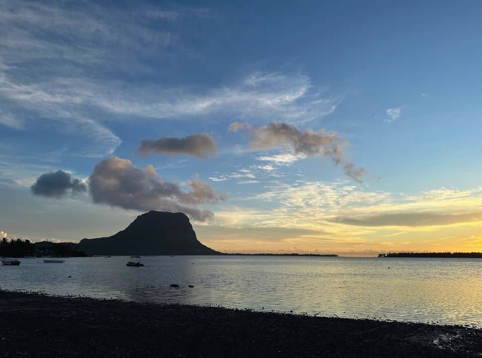 sun is setting at a beach in Mauritius, the yellow colored horizon is beautiful with the contour of a mountain and boats in the water