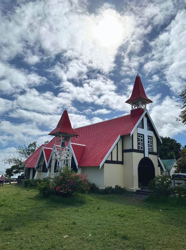 a beautiful church with a bright red roof and bell tower set in the grass, with in the back the ocean water in the north east of Mauiritius