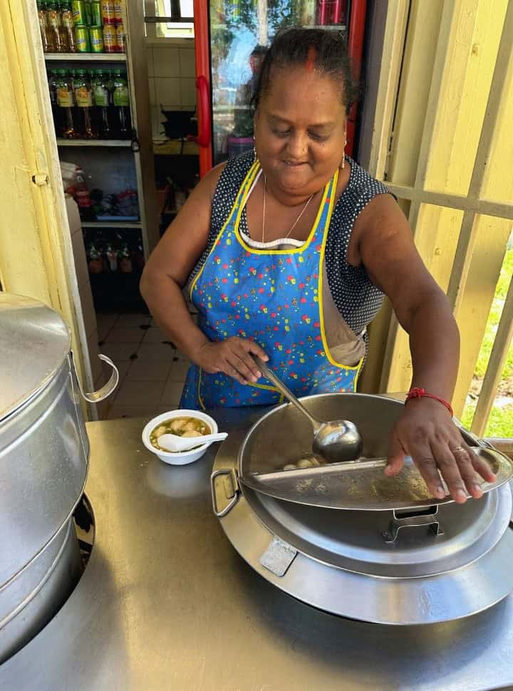 Mauritian lady preparing a soup dish with cheese balls in front of her shop in St. Felix Beach