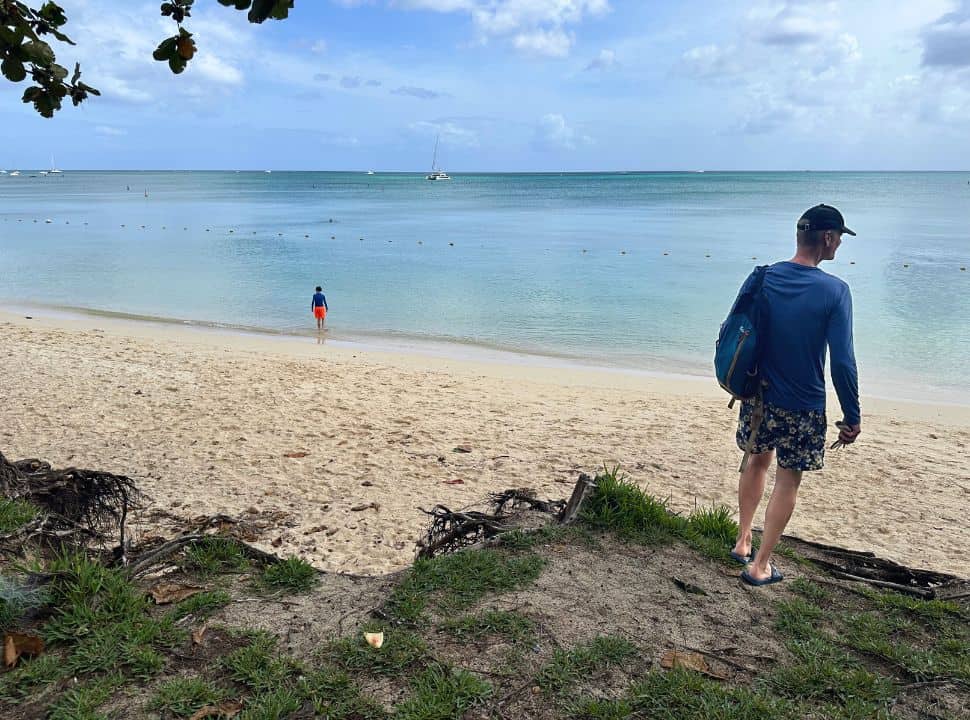 father and son arriving at a quiet beach called Mont Choisy in Mauritius, soft sanded sand, blue turquoise water and a sail boat in the distance