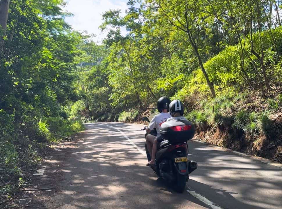 father and son on a motor scooter driving through the mountains with green vegetation in the south of Mauritius