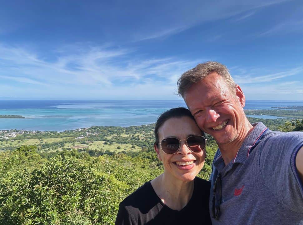 couple posing for a selfie with view of the green slopes and blue ocean of Mauritius