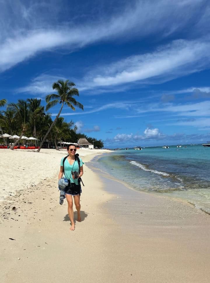 woman strolling along a white tropical beach called Le Morne in Mauritius with palm trees and clear blue ocean water