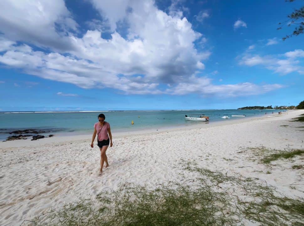 woman walking along a white soft sanded beach with turquoise water, a boat is anchored along the shore at palmar beach mauritius