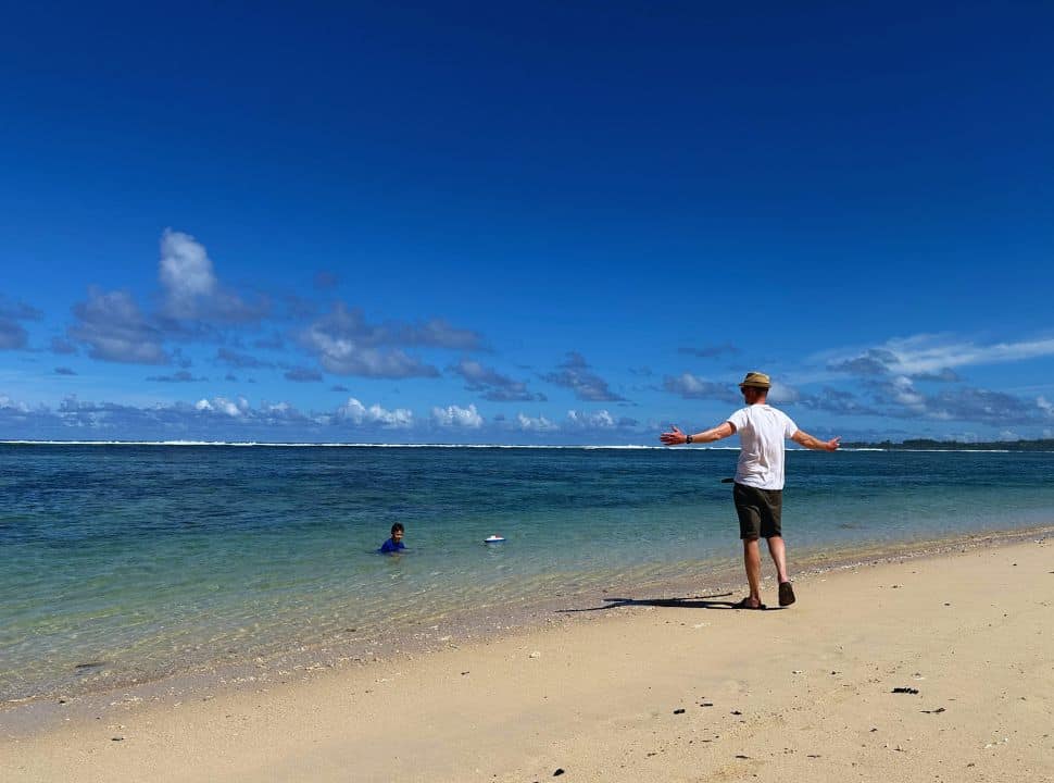 father standing along the ocean shore spreading his arms to take in the amazing beauty of the beach, son is playing with his boat in the water at Sint Felix Beach Mauritius