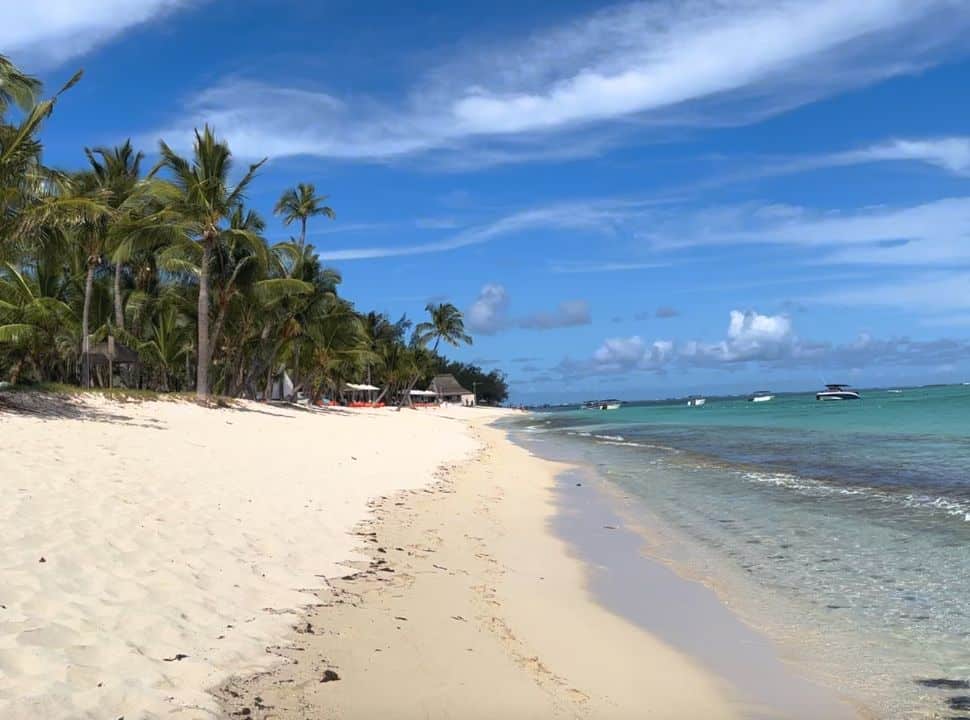 tropical beach with palm trees, white soft sand and turquoise water, boats anchored along the coast line and resort sun loungers are found in the shade and one of the best beaches in Mauritius