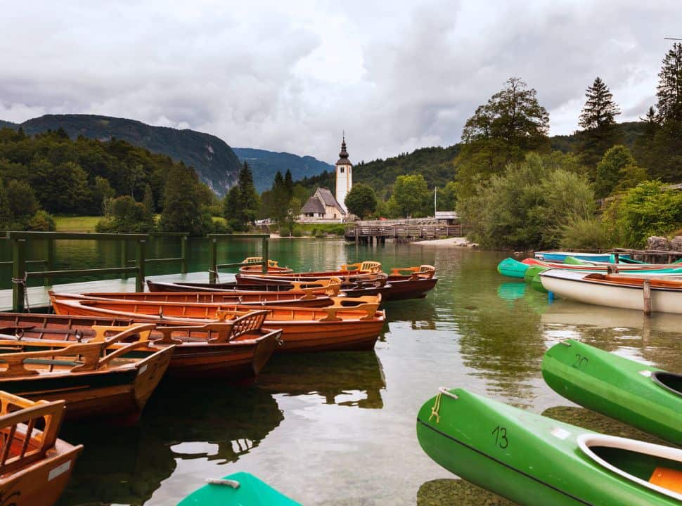 traditional wooden rowing boats and canoes docked at the lake Bohinj, with in the background the famous church set in Ribčev Laz 