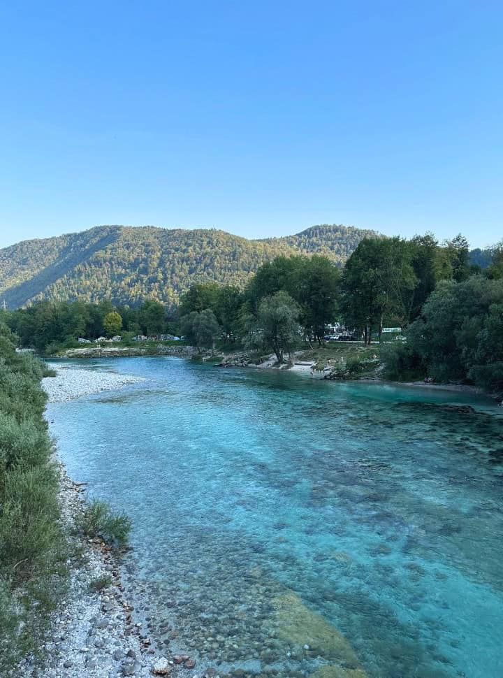 view of a campsite tucked under the trees, set along the blue Soča river