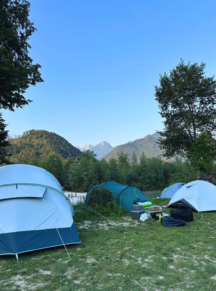 Tents pitched at a field right at the river front with views of impressive mountains in Tolmin Soca Valley Slovenia