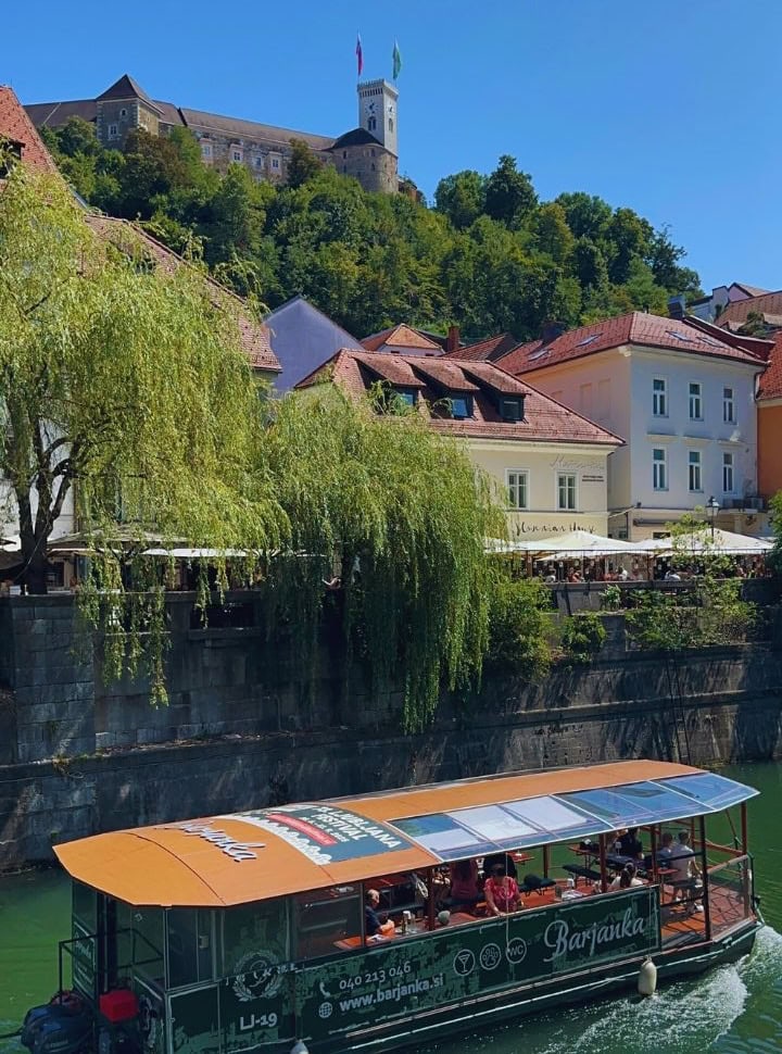 boat tour cruising through the river of Ljubliana, colourful houses are located along the river while the castle stands prominent on top of the hill