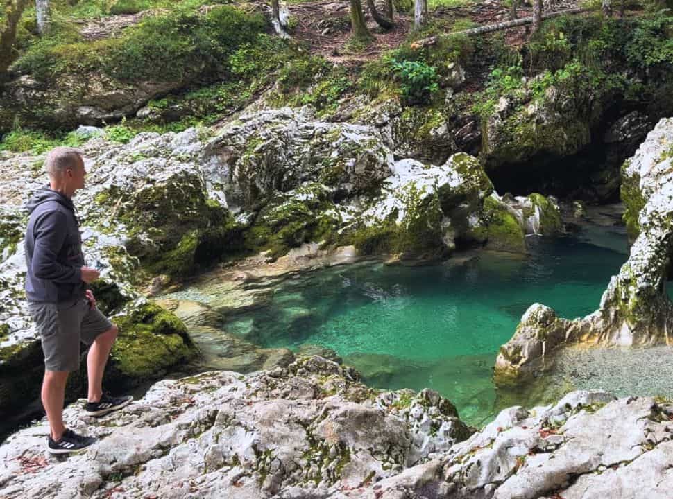 man looking out on the pool with crystal clear water located in one of the many gorges in Slovenia