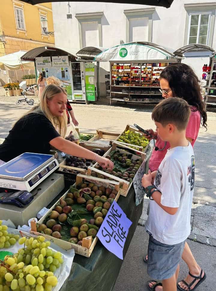 mother and son standing at a market stand while the seller is selecting figs for them in the capital city of Slovenia, Ljubljana. 