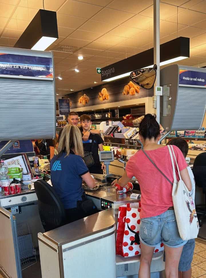 woman standing at the supermarket cashier packing the shopping in Slovenia, is expensive to visit?
